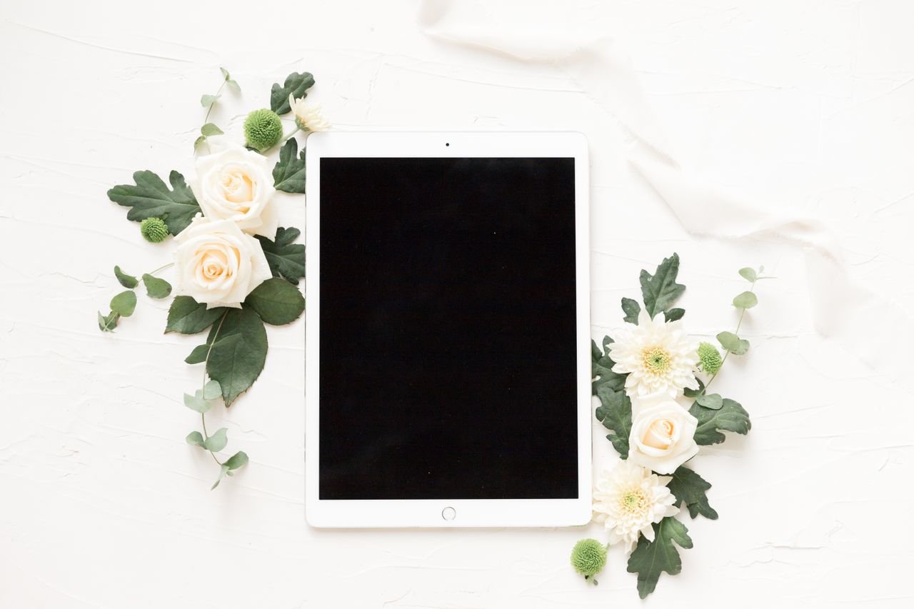 Stylish flatlay with white roses, chrysanthemums, and a digital tablet on a light background.